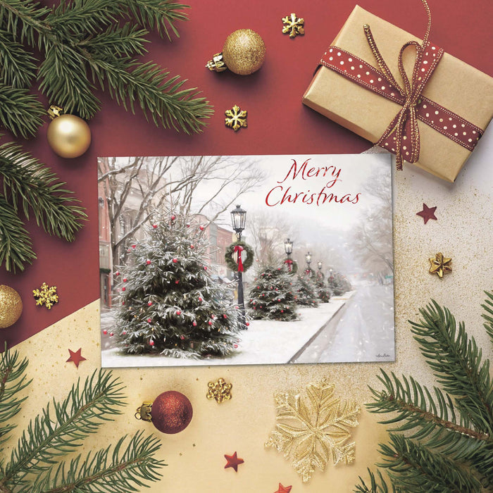 Christmas card with snowy street scene, surrounded by Christmas decorations like gold balls, greenery, and a gift.