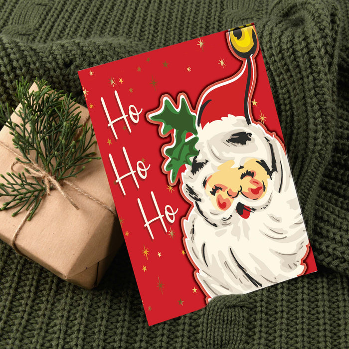 Red Christmas card with Santa Claus design on a green textured surface with a gift.