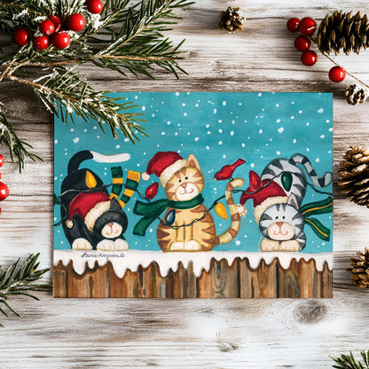 Christmas-themed card with cats and holiday decorations on a wooden surface.