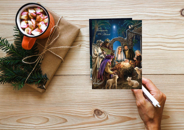 Hand holding a Christmas card with a nativity scene on a wooden table with a mug and gift.